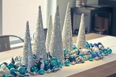 several silver christmas trees on a table with blue and white ornaments in front of them