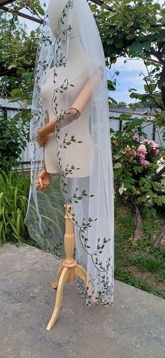 a mannequin wearing a veil and dress on a wooden stand in front of some bushes