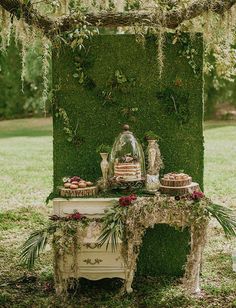 a table topped with cakes and desserts under a lush green canopy covered in moss