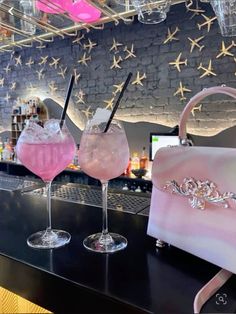 two pink cocktails sitting on top of a bar next to a purse and drink glasses