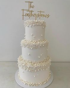 a three tiered white wedding cake with pearls on the bottom and gold topper