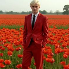 a man in a red suit and tie standing in a field full of orange flowers