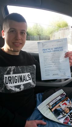 a young man sitting in the back seat of a car holding up a piece of paper