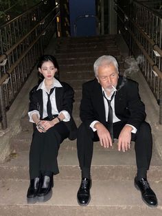 two people dressed in suits sitting on steps with their feet propped against the railings