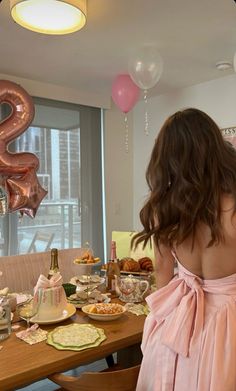 a woman standing in front of a table filled with food and balloons that are shaped like the number two