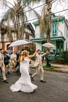 a bride and groom dancing in the street with their umbrellas open as people walk by