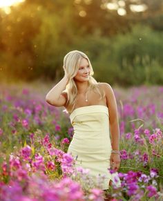 a woman standing in a field of flowers with her hand on her head and looking at the camera