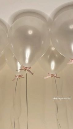 three white balloons with pink bows tied to them