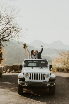 a bride and groom standing in the back of a white jeep with their arms up