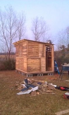 a small wooden shed sitting on top of a grass covered field next to a pile of wood