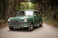 an old green car is parked on the side of the road in front of some trees