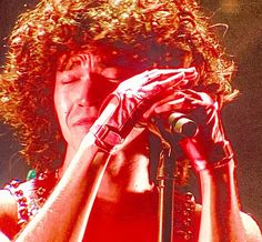 a man with curly hair holding a microphone in front of his face as he sings