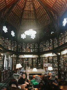 people sitting at tables in a library with lots of books on the walls and ceiling