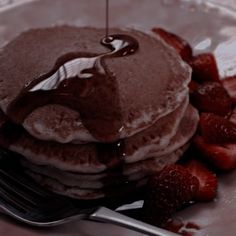 a stack of pancakes with syrup and strawberries on a plate next to a fork