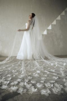 a woman in a wedding dress is standing on some stairs with her veil over her head