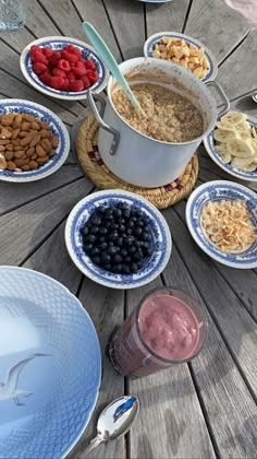 a wooden table topped with plates and bowls filled with cereal, fruit and veggies