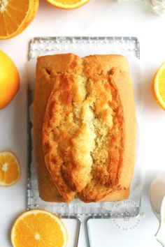 a loaf of orange bread sitting on top of a cooling rack next to sliced oranges