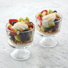 two clear bowls filled with fruit and yogurt on top of a marble counter