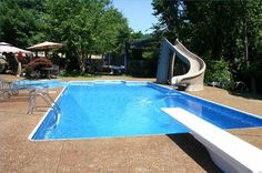 an empty swimming pool with a slide in the back ground and chairs around it, on a sunny day