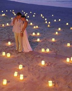 two people standing in the sand surrounded by candles