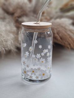 a glass jar with a straw sticking out of the lid and flowers painted on it