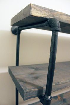 a wooden shelf with metal pipes and brackets on the top, against a white wall