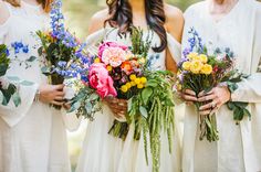 three bridesmaids in white dresses holding bouquets of colorful flowers and greenery