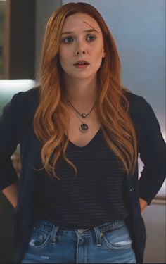 a woman with long red hair wearing jeans and a black shirt is looking at the camera