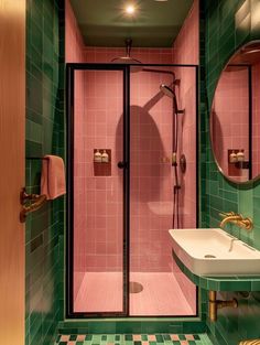 a bathroom with green and pink tiles on the walls, shower stall, sink and mirror