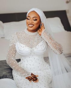 a woman sitting on top of a bed wearing a white dress and headpieces