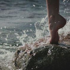 a person standing on top of a rock in the water with their feet sticking out