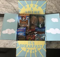 an open box filled with food on top of a marble countertop next to a sign that says rise and shine it's breakfast time