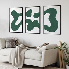 two green and white paintings hang on the wall next to a couch in a living room