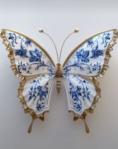 a blue and white butterfly with gold trim on it's wings is hanging from the wall