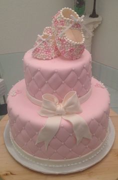 a pink and white cake with baby shoes on the top, sitting on a table