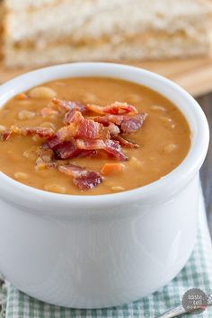 a bowl of soup with bacon and bread in the background