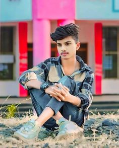 a young man sitting on the ground in front of a building with his hands crossed