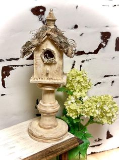 a bird house sitting on top of a wooden table next to a vase with flowers