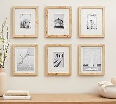 there are many framed pictures on the wall above a table with vases and books