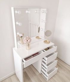 a white dressing table with drawers and a mirror on the wall above it that has lights