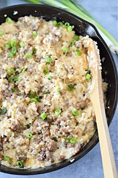 a skillet filled with rice, meat and green onions next to a wooden spoon