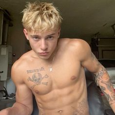 a shirtless young man with tattoos on his chest sitting in front of a motorcycle