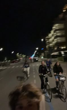 a group of people riding bikes down a street at night with buildings in the background