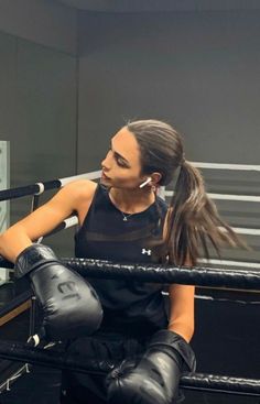 a woman sitting on top of a boxing ring wearing black gloves and holding a microphone