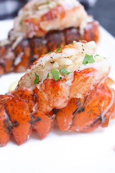 two pieces of cooked lobster on a white plate with garnish and parsley