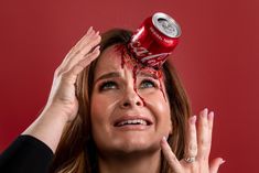 a woman holding a can of coca - cola up to her head with blood on it