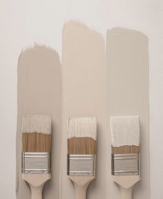 three paintbrushes are lined up against the wall with different shades of white on them