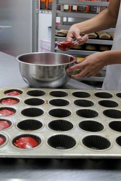 a person in an industrial kitchen making cupcakes with red icing on them