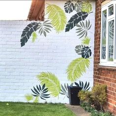 a white brick building with green leaves painted on it's side and grass in front