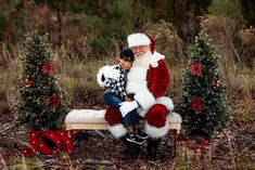 a boy sitting on a bench with santa claus next to christmas trees in the woods